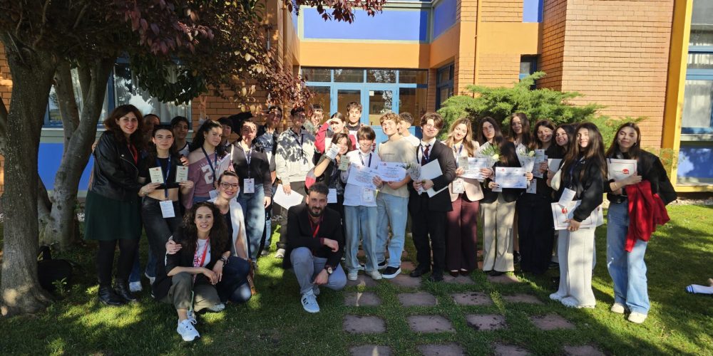 Group of students posing outside a brick building, many holding certificates and wearing lanyards on a sunny day.