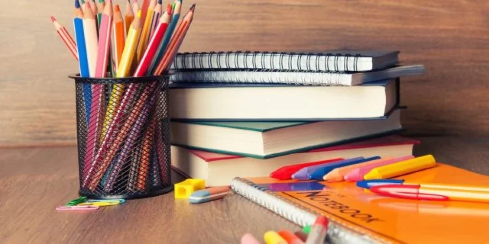 Desk with a mesh cup of colored pencils, stacked notebooks, rulers, and pens.